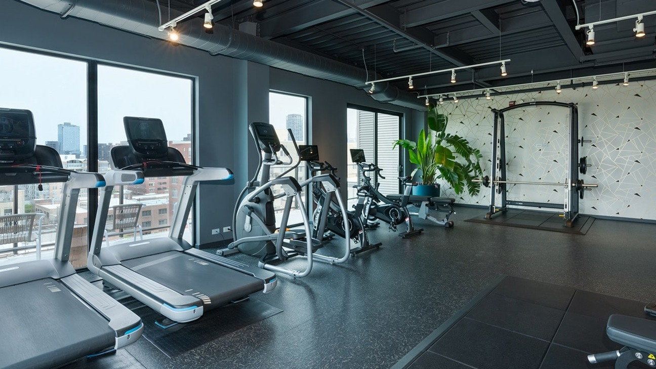 Modern gym at The Jax in Chicago, featuring a range of cardio equipment, strength machines, and large windows with city views