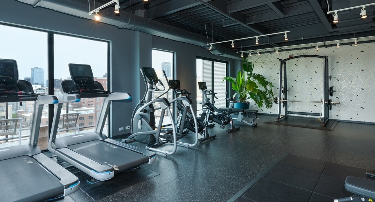 Modern gym at The Jax in Chicago, featuring a range of cardio equipment, strength machines, and large windows with city views