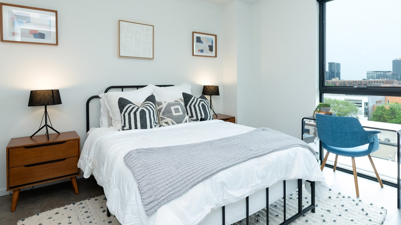 Cozy apartment bedroom at The Jax in Chicago, featuring a comfortable bed, stylish decor, and a dedicated desk area with city views