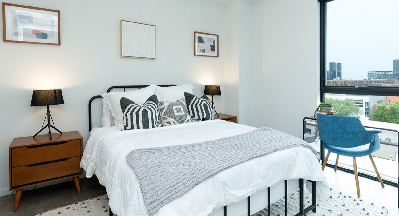 Cozy apartment bedroom at The Jax in Chicago, featuring a comfortable bed, stylish decor, and a dedicated desk area with city views