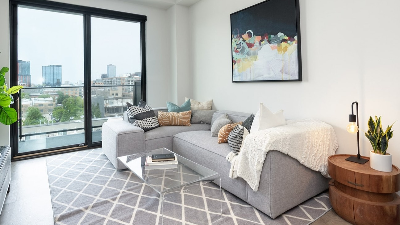 Bright living room at The Jax in Chicago, featuring a comfortable sectional sofa, modern art, and a balcony with city views