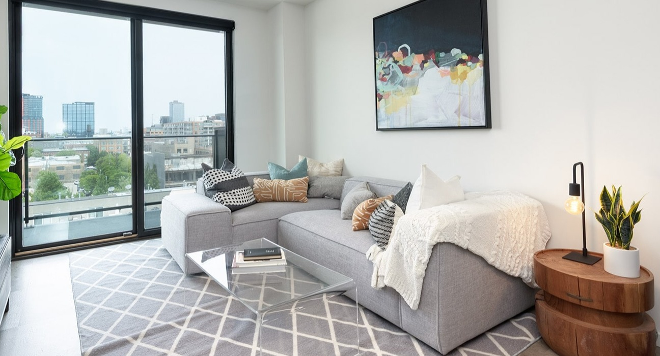 Bright living room at The Jax in Chicago, featuring a comfortable sectional sofa, modern art, and a balcony with city views