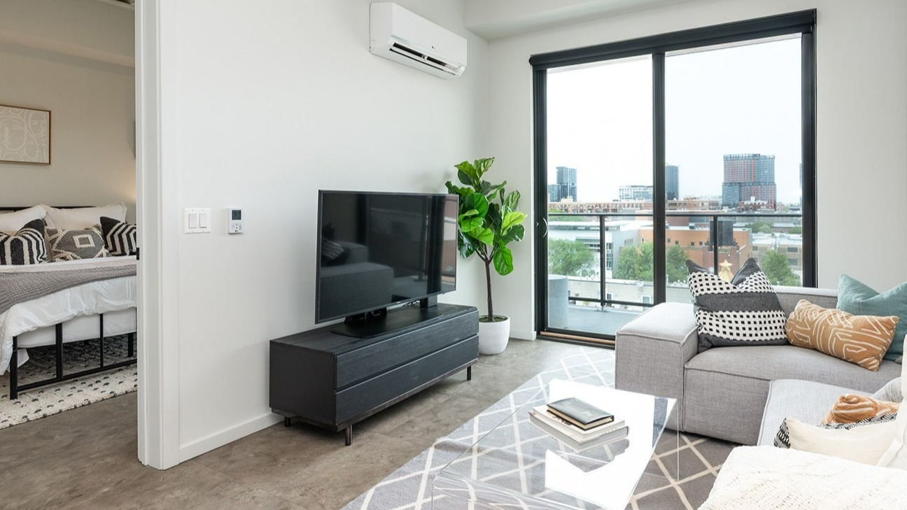 Open-concept living room at The Jax in Chicago, offering a view into a cozy bedroom, with modern decor and city views