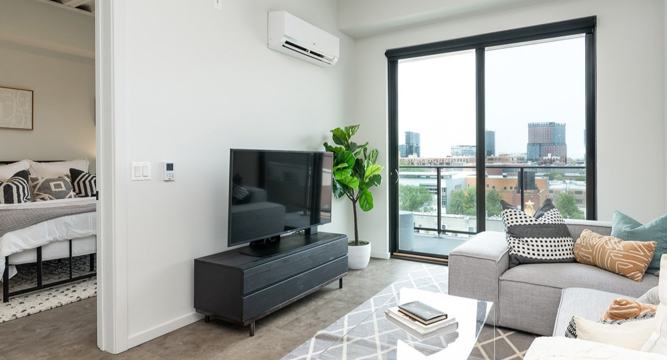 Open-concept living room at The Jax in Chicago, offering a view into a cozy bedroom, with modern decor and city views