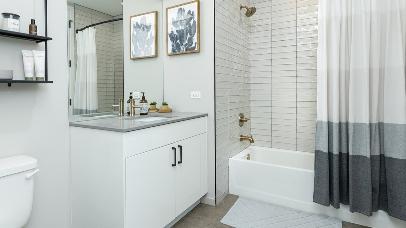 Modern apartment bathroom at The Jax in Chicago, featuring a sleek white vanity, large mirror, and a bathtub with shower