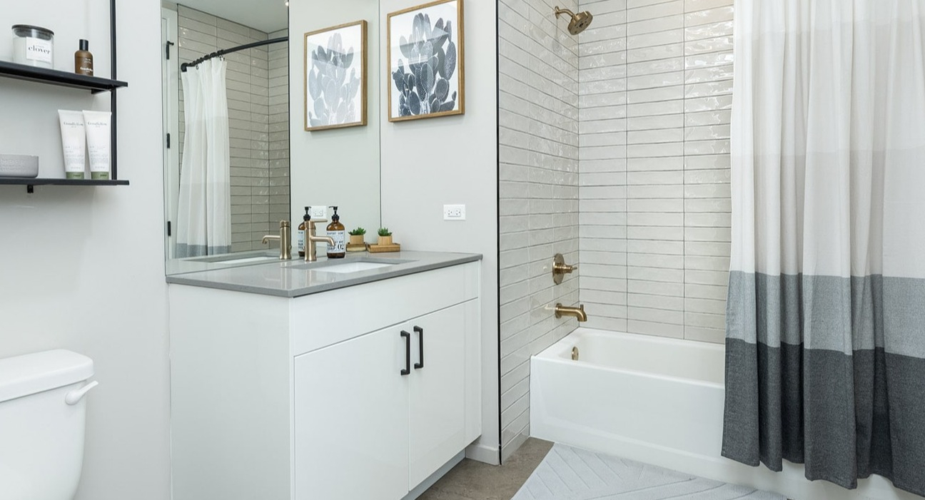 Modern apartment bathroom at The Jax in Chicago, featuring a sleek white vanity, large mirror, and a bathtub with shower