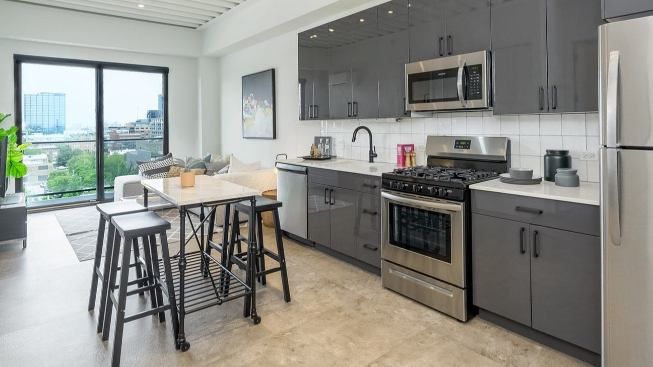Modern kitchen at The Jax in Chicago, featuring sleek gray cabinetry, stainless steel appliances, and a compact dining area