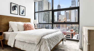 Inviting master bedroom at The Leo in Chicago, featuring a wooden bed frame, cozy bedding, and stunning city views