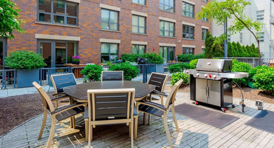 A charming outdoor courtyard area featuring a dining table with chairs and a barbecue grill at The Madison at Racine in Chicago