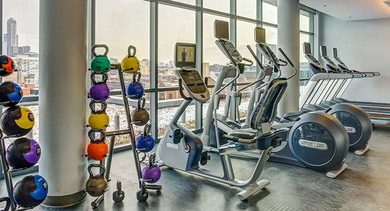 A bright, modern fitness center with various cardio machines, free weights, and large windows offering city views at The Madison at Racine