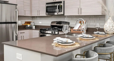 A sleek apartment kitchen equipped with stainless steel appliances, light wood cabinetry, and a spacious island with bar seating at The Madison at Racine