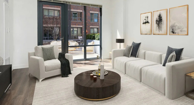 A bright, modern living room with comfortable white furniture, a large rug, and direct access to an outdoor balcony at The Madison at Racine in Chicago