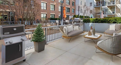 An inviting outdoor patio space with a BBQ grill, comfortable seating, and lush landscaping at The Madison at Racine apartments in Chicago