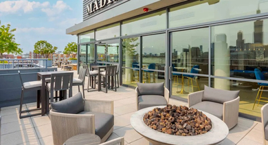 A luxurious rooftop lounge area with stylish outdoor seating and a modern fire pit, offering cityscape views at The Madison at Racine in Chicago