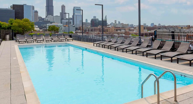 A sparkling rooftop swimming pool with lounge chairs, offering stunning panoramic views of the Chicago city skyline at The Madison at Racine