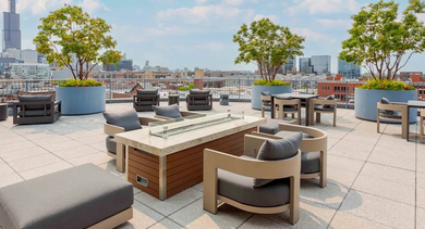 An expansive rooftop deck with various seating arrangements, mature trees in planters, and panoramic views of the Chicago skyline at The Madison at Racine