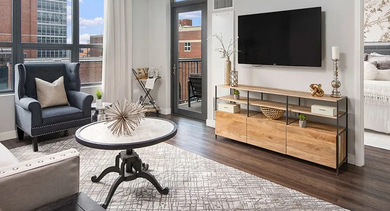 A comfortable and spacious living room with dark hardwood floors, a large TV, and access to an outdoor balcony at The Madison at Racine in Chicago