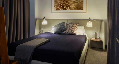 A comfortable and modern bedroom featuring a upholstered headboard, soft lighting, and dark curtains, perfect for relaxation at The Mason in Chicago