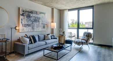 A spacious living room with an exposed concrete ceiling, hardwood floors, a comfortable sofa, and large windows bringing in natural light at The Mason in Chicago