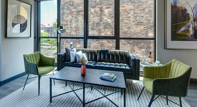 A modern living room with exposed concrete ceilings, a sleek sofa, accent chairs, and large windows providing urban views at The Mason in Chicago