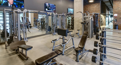 A spacious and modern fitness center with weight machines, free weights, cardio equipment, and large mirrors at The Mason in Chicago