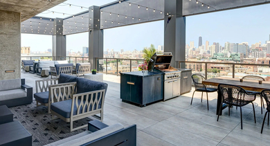 An expansive rooftop deck featuring outdoor dining tables, lounge seating areas, and a modern barbecue grill station at The Mason in Chicago