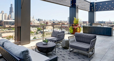 An inviting rooftop lounge with comfortable seating, string lights, a grill station, and stunning Chicago skyline views at The Mason