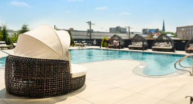 A vibrant rooftop swimming pool surrounded by comfortable lounge chairs and private cabanas, under a clear sky at The Mason in Chicago