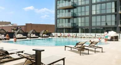 A refreshing rooftop swimming pool with lounge seating, offering views of the surrounding city buildings and blue sky at The Mason in Chicago