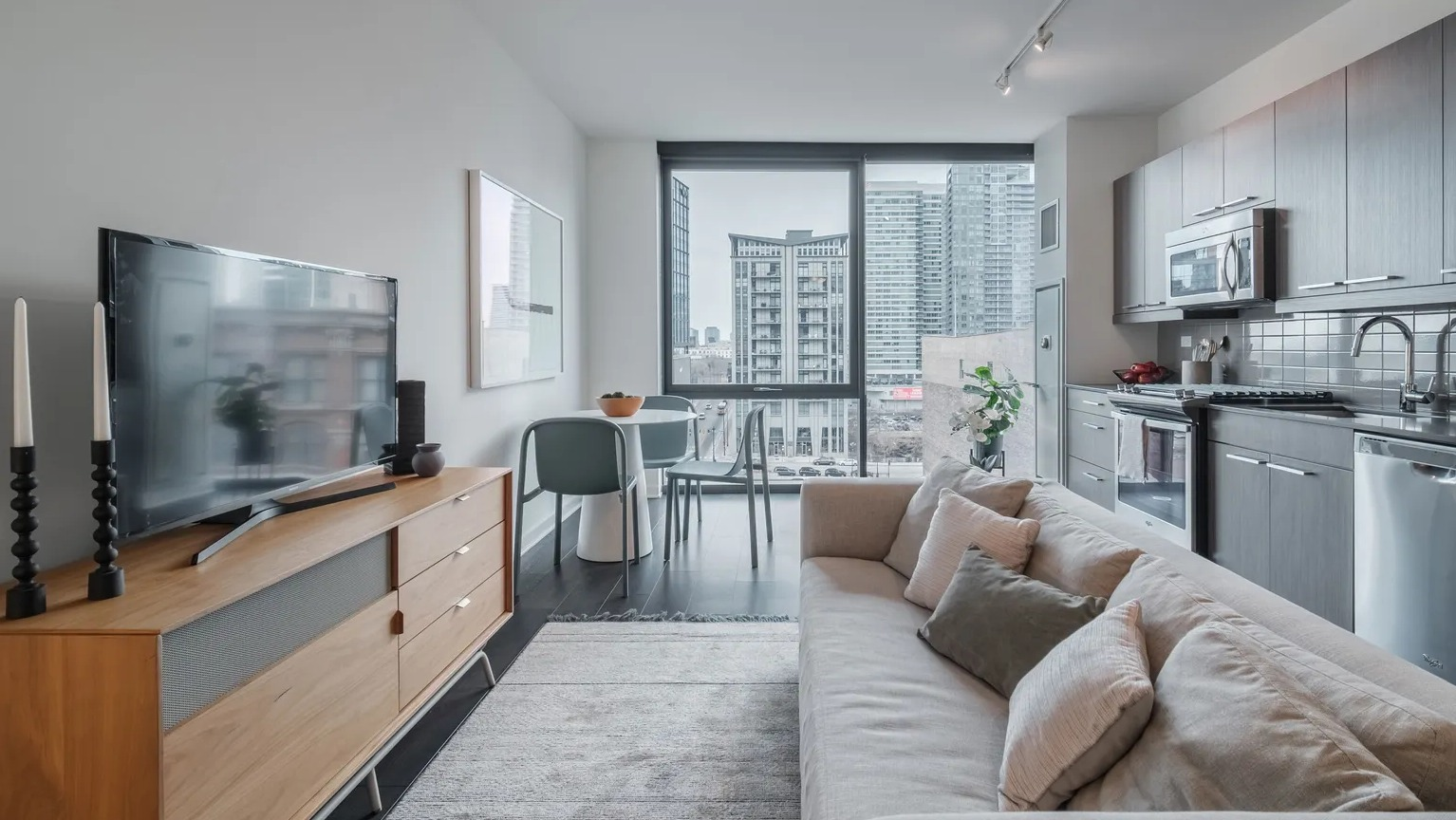A cozy and modern apartment living room connected to a kitchen, featuring light furniture, a TV, and urban views at The Parker Fulton Market in Chicago