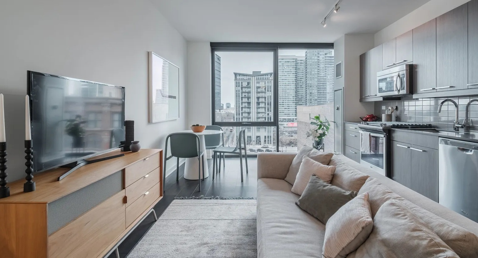 A cozy and modern apartment living room connected to a kitchen, featuring light furniture, a TV, and urban views at The Parker Fulton Market in Chicago
