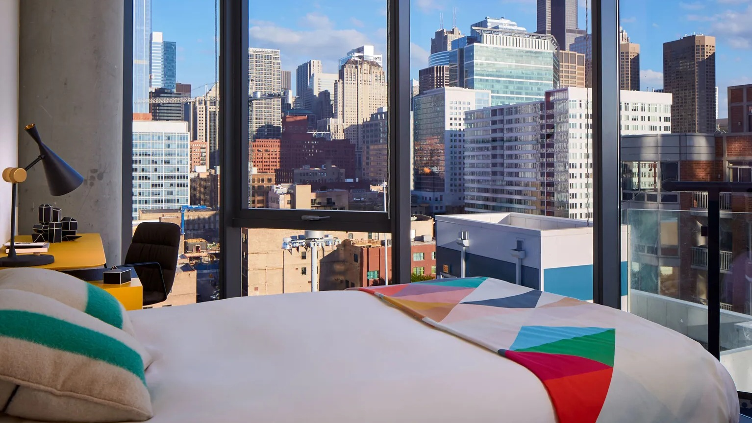A vibrant and chic bedroom with a comfortable bed, colorful accents, and a breathtaking panoramic view of the Chicago skyline at The Parker Fulton Market