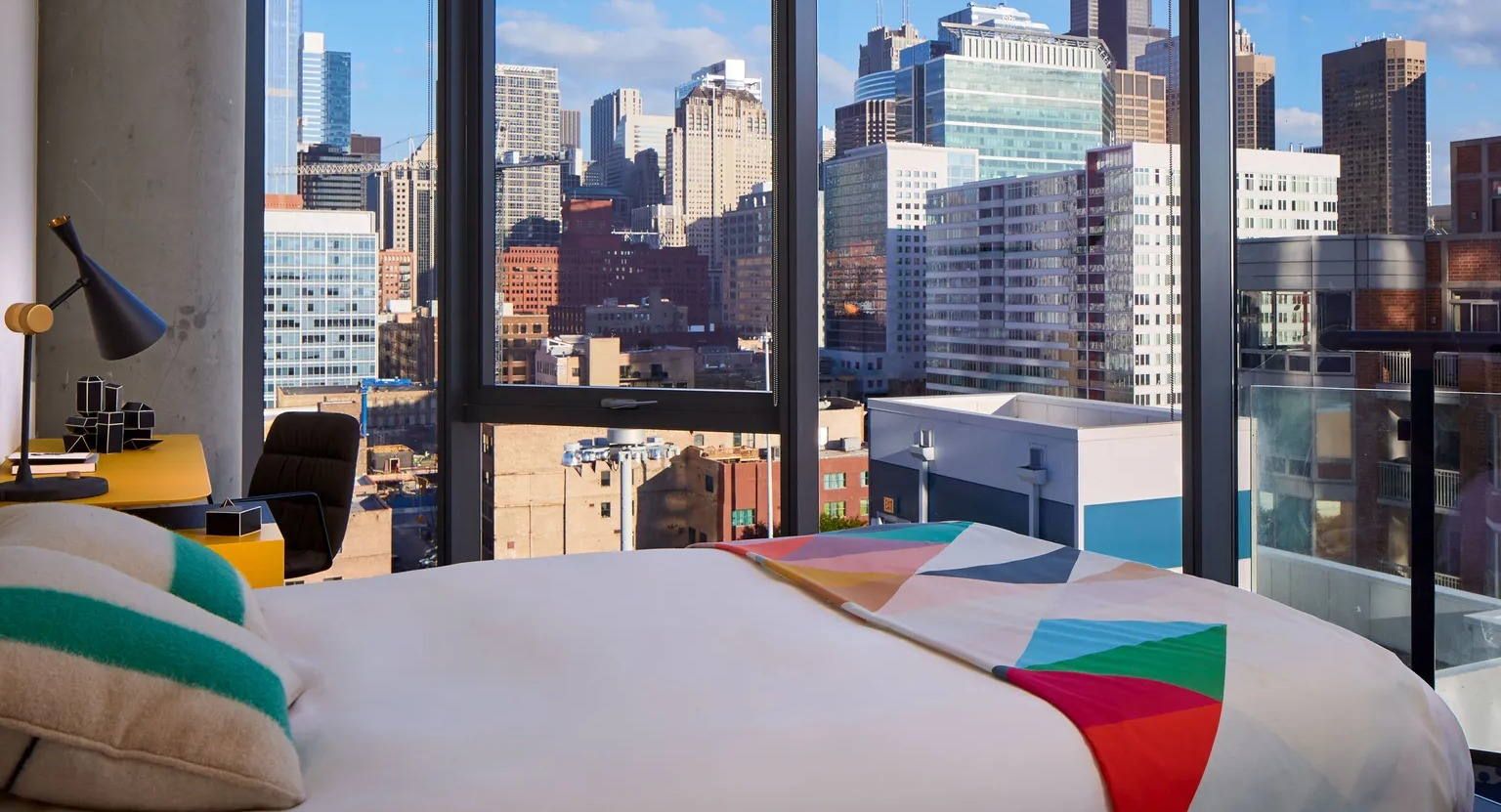 A vibrant and chic bedroom with a comfortable bed, colorful accents, and a breathtaking panoramic view of the Chicago skyline at The Parker Fulton Market
