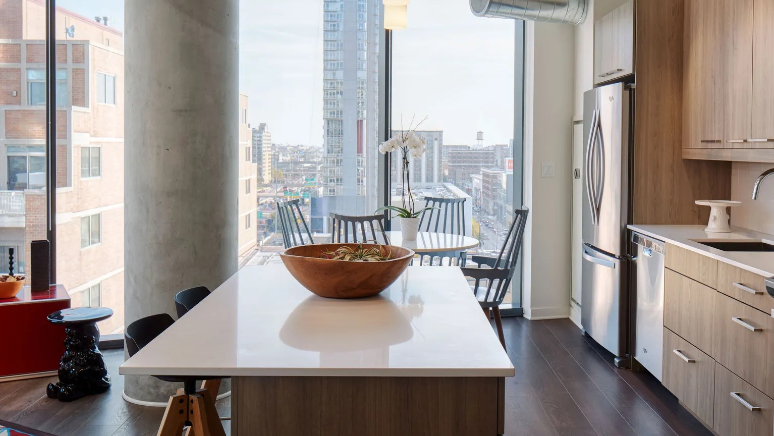 A contemporary kitchen with light wood cabinets, stainless steel appliances, a large island, and expansive city views from floor-to-ceiling windows at The Parker Fulton Market