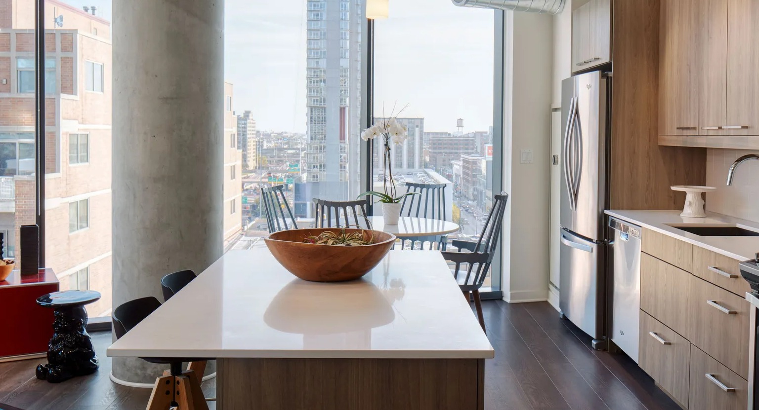 A contemporary kitchen with light wood cabinets, stainless steel appliances, a large island, and expansive city views from floor-to-ceiling windows at The Parker Fulton Market