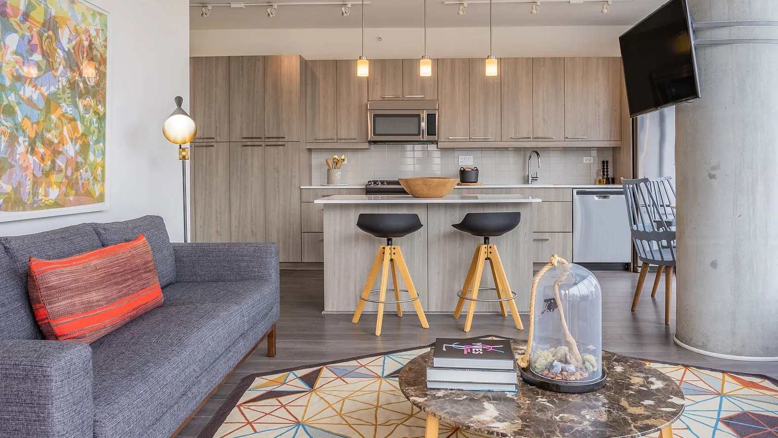 A vibrant and modern living room connected to a kitchen, featuring a comfortable sofa, an eye-catching rug, and a television at The Parker Fulton Market in Chicago