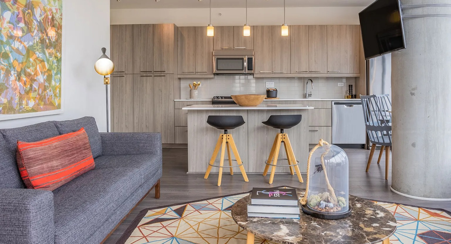 A vibrant and modern living room connected to a kitchen, featuring a comfortable sofa, an eye-catching rug, and a television at The Parker Fulton Market in Chicago