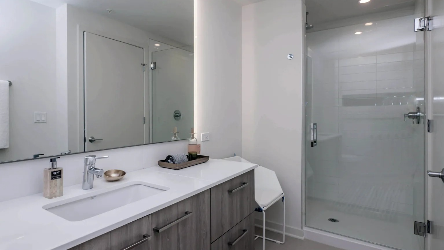 A contemporary bathroom with a spacious walk-in shower, a large vanity with a lighted mirror, and sleek fixtures at The Parker Fulton Market in Chicago