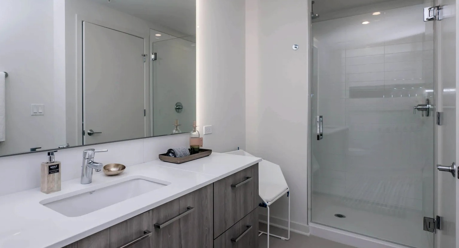 A contemporary bathroom with a spacious walk-in shower, a large vanity with a lighted mirror, and sleek fixtures at The Parker Fulton Market in Chicago