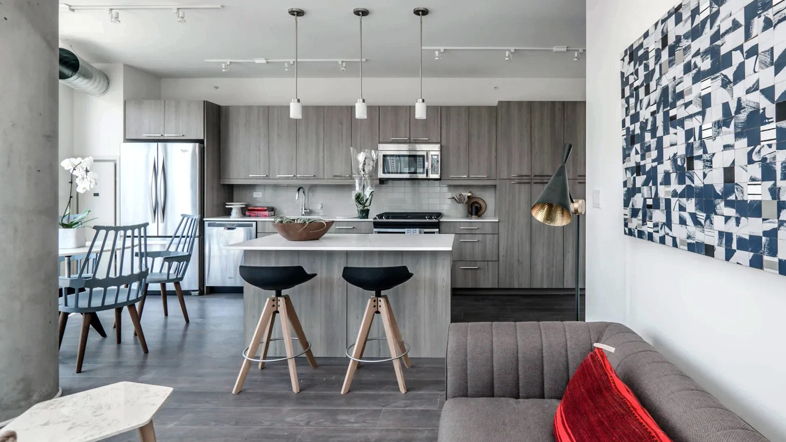 A modern open-concept living room and kitchen area with stylish decor, a comfortable sofa, and a kitchen island with stools at The Parker Fulton Market in Chicago