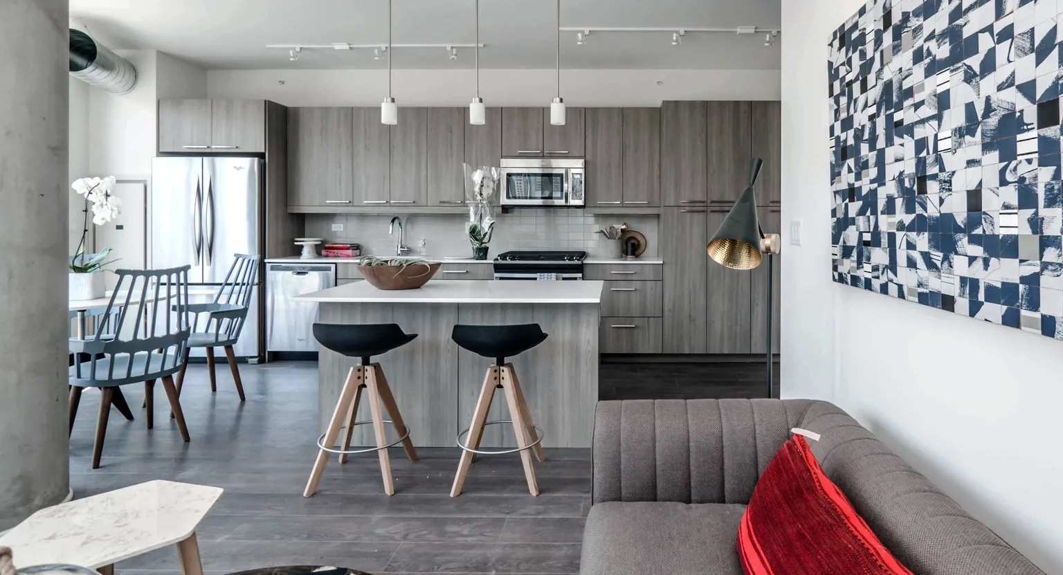 A modern open-concept living room and kitchen area with stylish decor, a comfortable sofa, and a kitchen island with stools at The Parker Fulton Market in Chicago