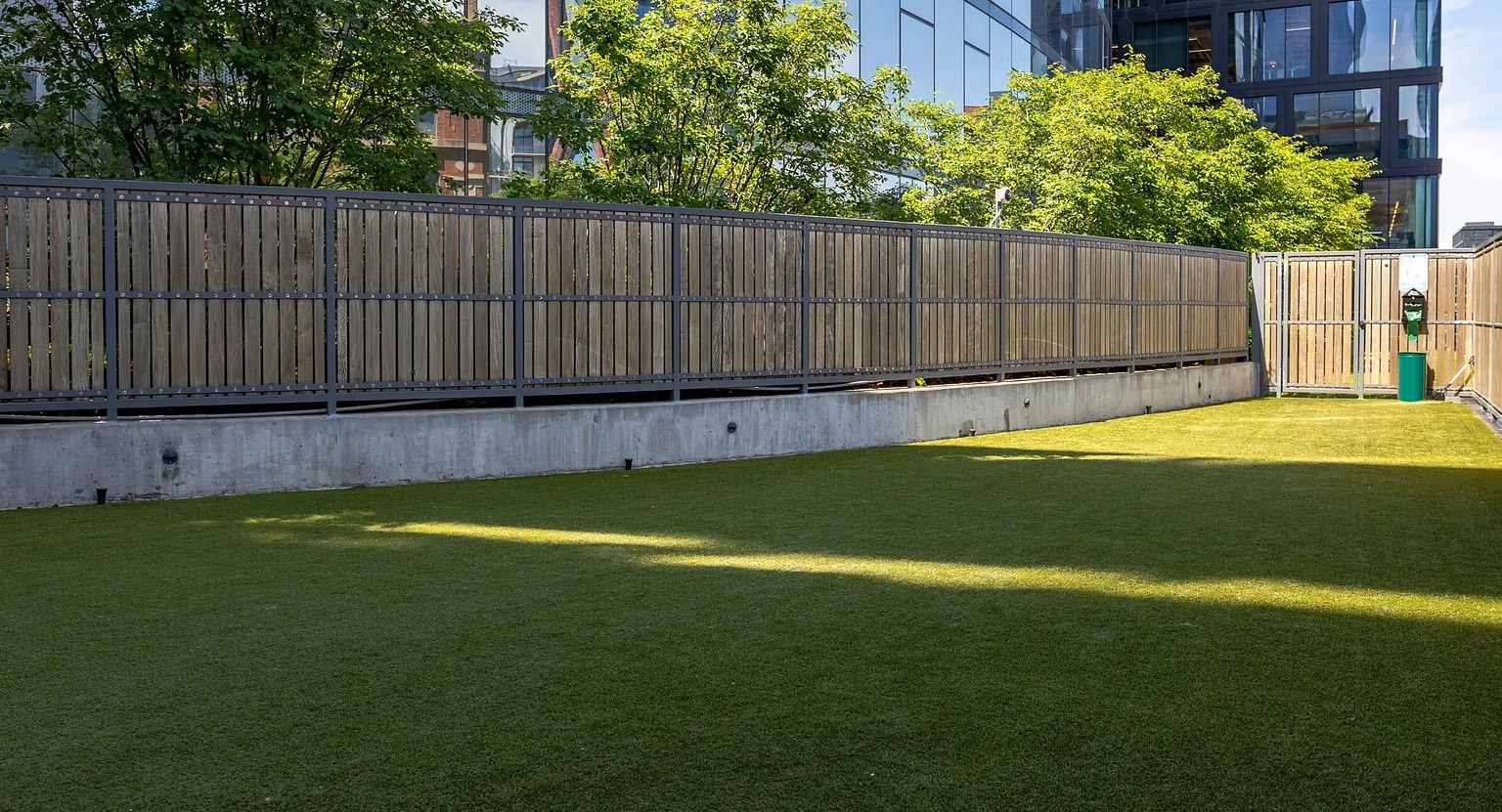 A spacious and well-maintained outdoor dog park with artificial turf and a wooden fence, ideal for pets at The Parker Fulton Market in Chicago