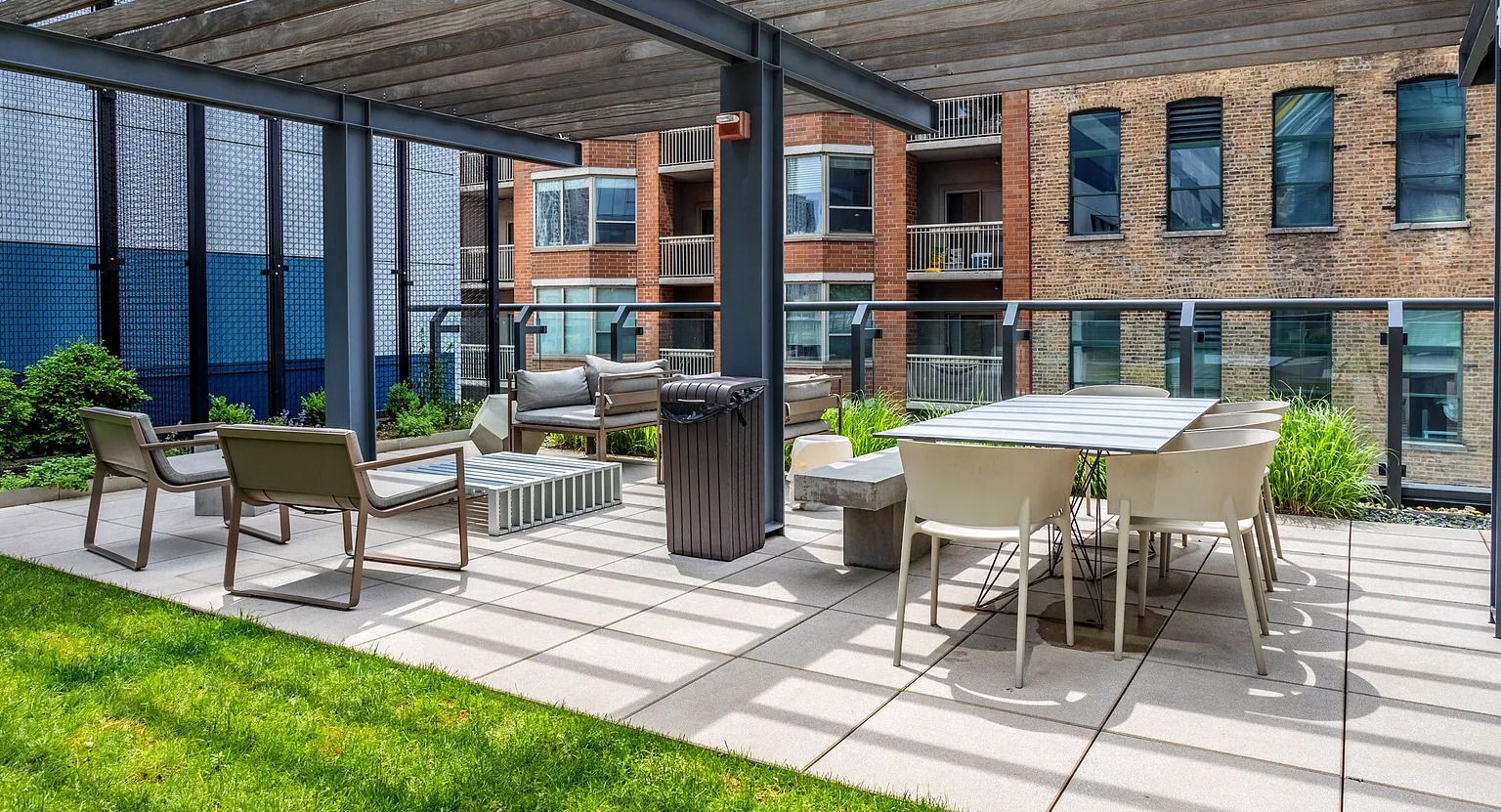 A charming outdoor patio area with a modern pergola, dining table, and lounge seating, surrounded by green landscaping at The Parker Fulton Market in Chicago