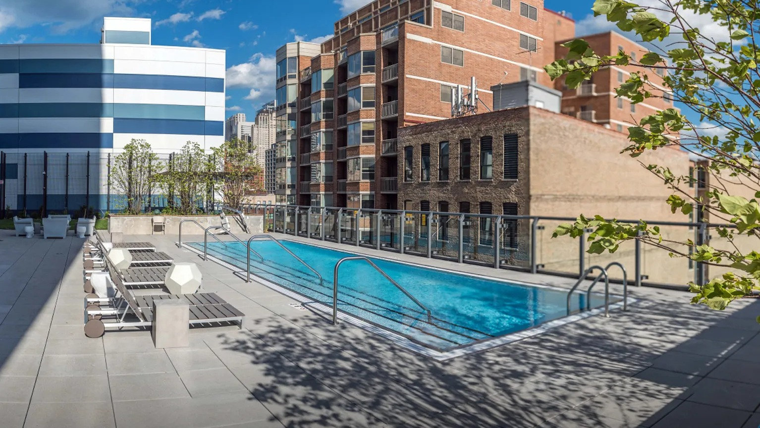 A refreshing rooftop swimming pool with lounge chairs, surrounded by the cityscape and green landscaping at The Parker Fulton Market in Chicago