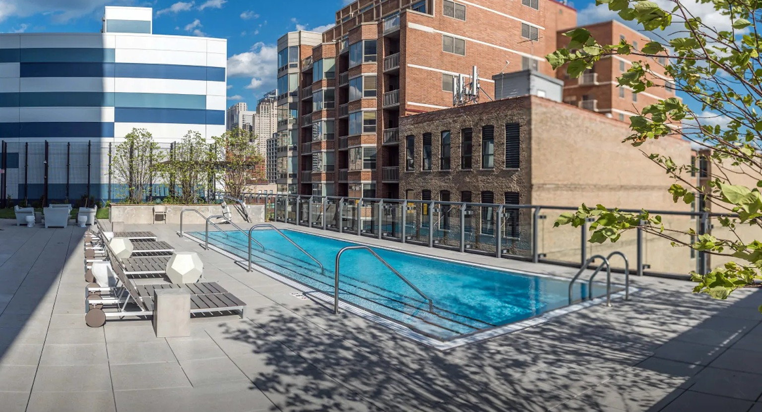 A refreshing rooftop swimming pool with lounge chairs, surrounded by the cityscape and green landscaping at The Parker Fulton Market in Chicago