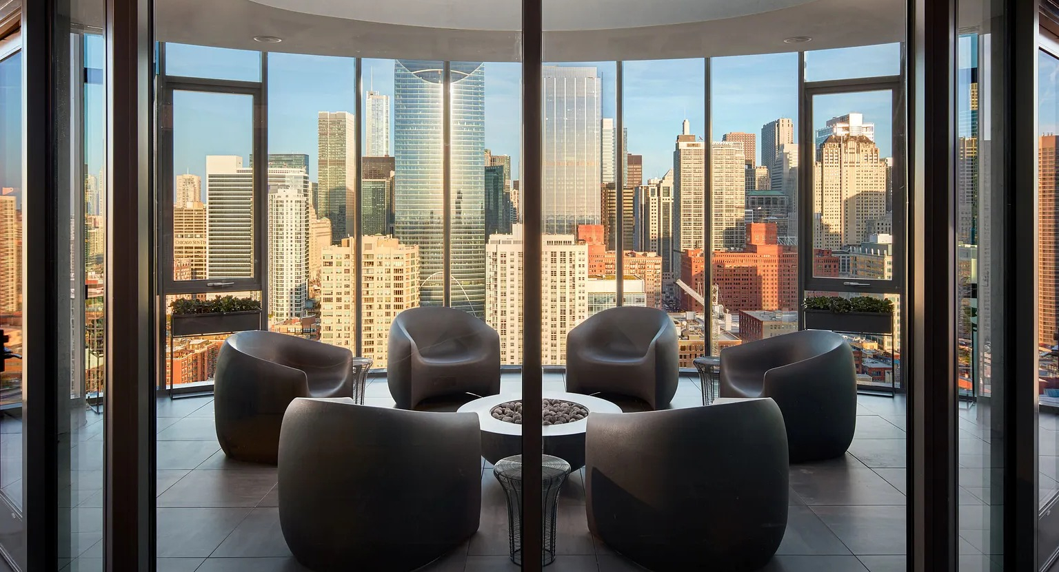 An elegant rooftop sky lounge with modern seating arranged around a fire pit, offering spectacular panoramic views of the Chicago skyline at The Parker Fulton Market