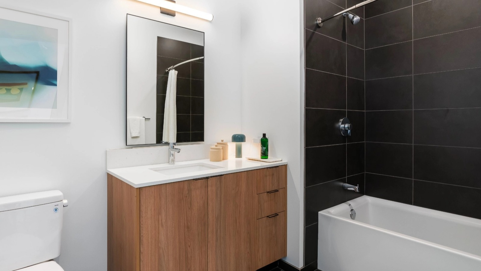 A bright and contemporary bathroom with a bathtub/shower combo featuring dark subway tiles, a stylish vanity, and modern lighting at The Reed in Chicago