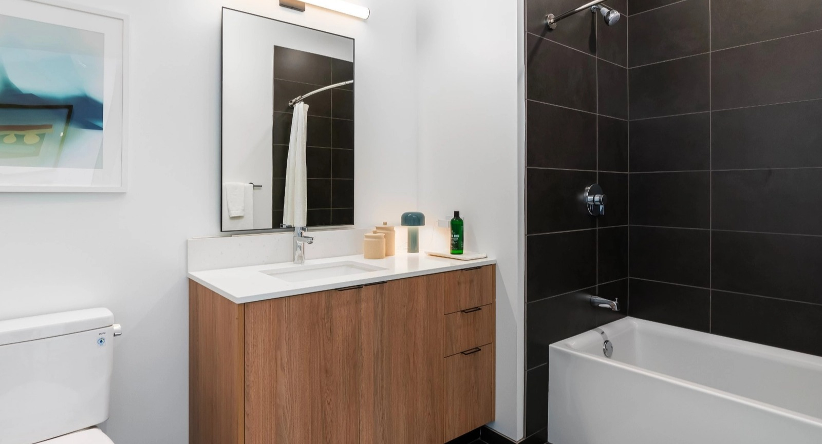 A bright and contemporary bathroom with a bathtub/shower combo featuring dark subway tiles, a stylish vanity, and modern lighting at The Reed in Chicago
