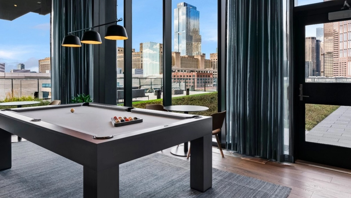A sophisticated game room featuring a billiards table, stylish curtains, and expansive windows with incredible Chicago skyline views at The Reed in Chicago