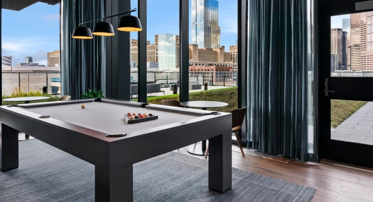 A sophisticated game room featuring a billiards table, stylish curtains, and expansive windows with incredible Chicago skyline views at The Reed in Chicago